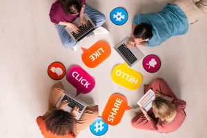 Overview of four young contemporary friends using mobile gadgets on the floor